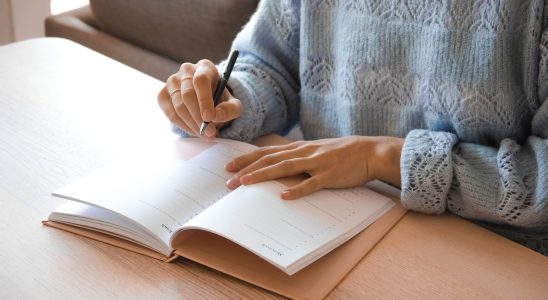 woman in white and gray sweater writing on white paper