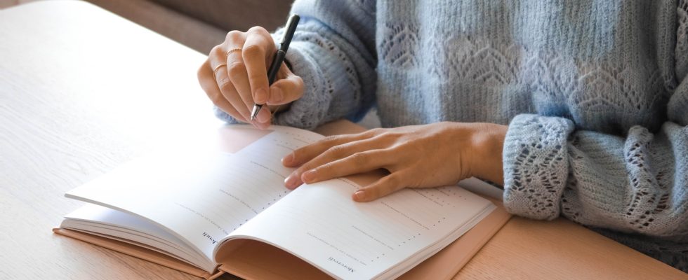 woman in white and gray sweater writing on white paper